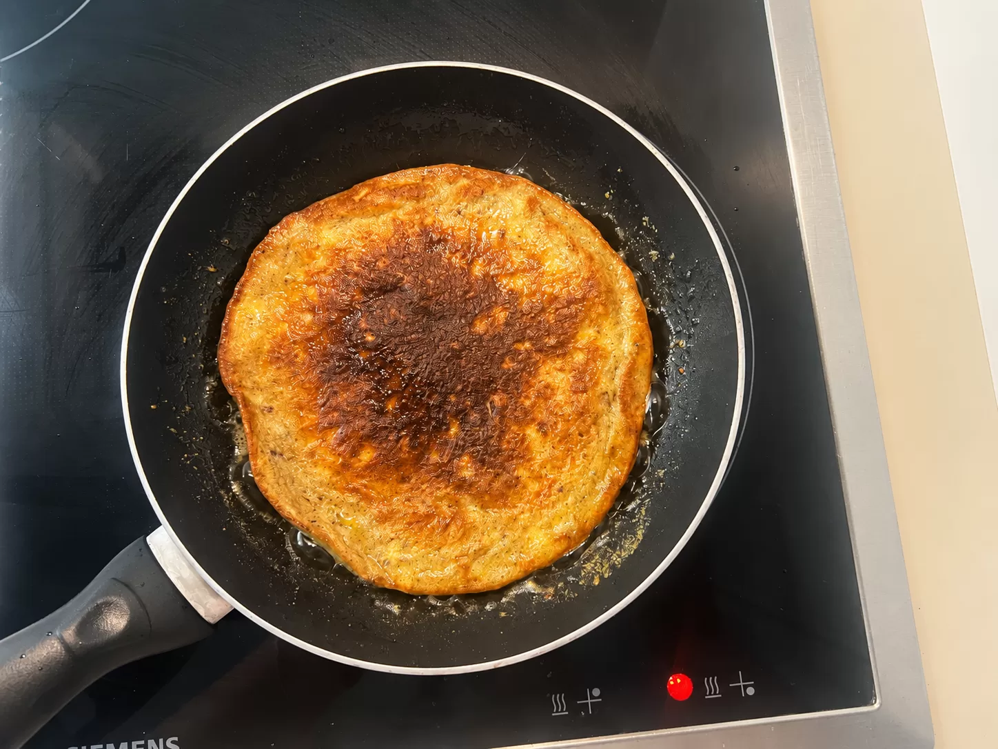A banana pancake being flipped after the underside has turned golden brown.