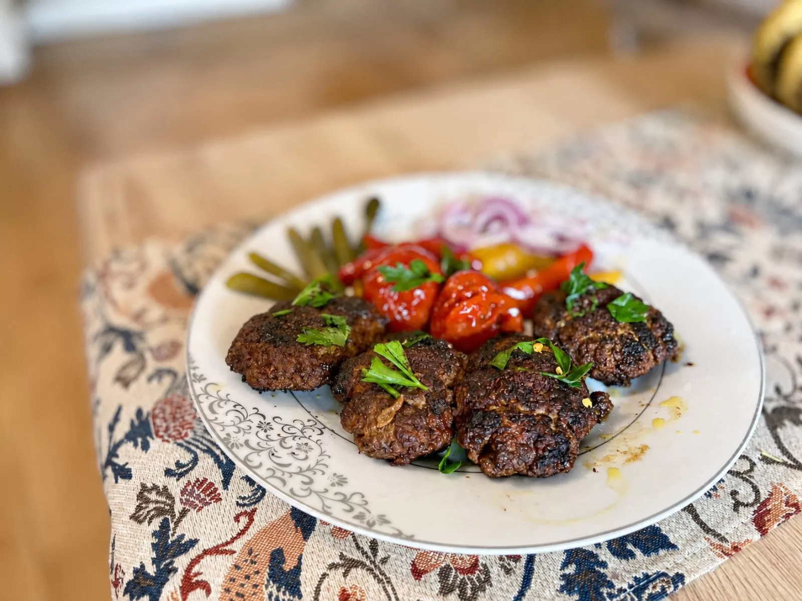 Persian Kabab Tabei served with charred tomato halves, sliced red onion, fresh parsley, lengthwise-cut pickles and lemon wedges, finished with sumac.